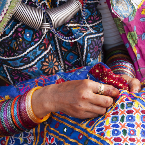 Tribal women sewing ethnic and traditional hand embroidered dresses in front of their hut, Gujarat, India.